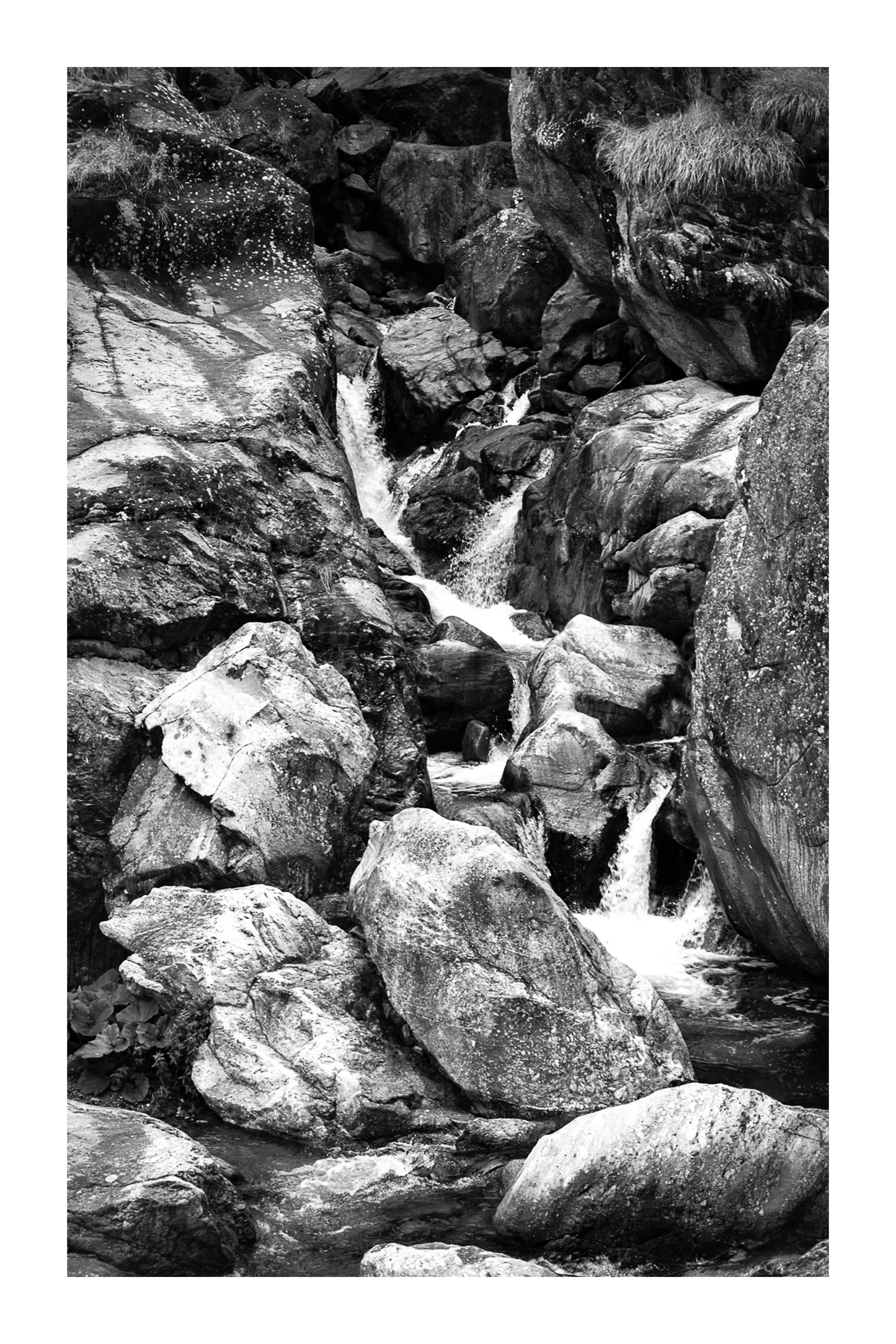 Cascade du Ray entre de gros blocs rocheux, eau qui s’écoule en marches successives, noir et blanc avec bordure