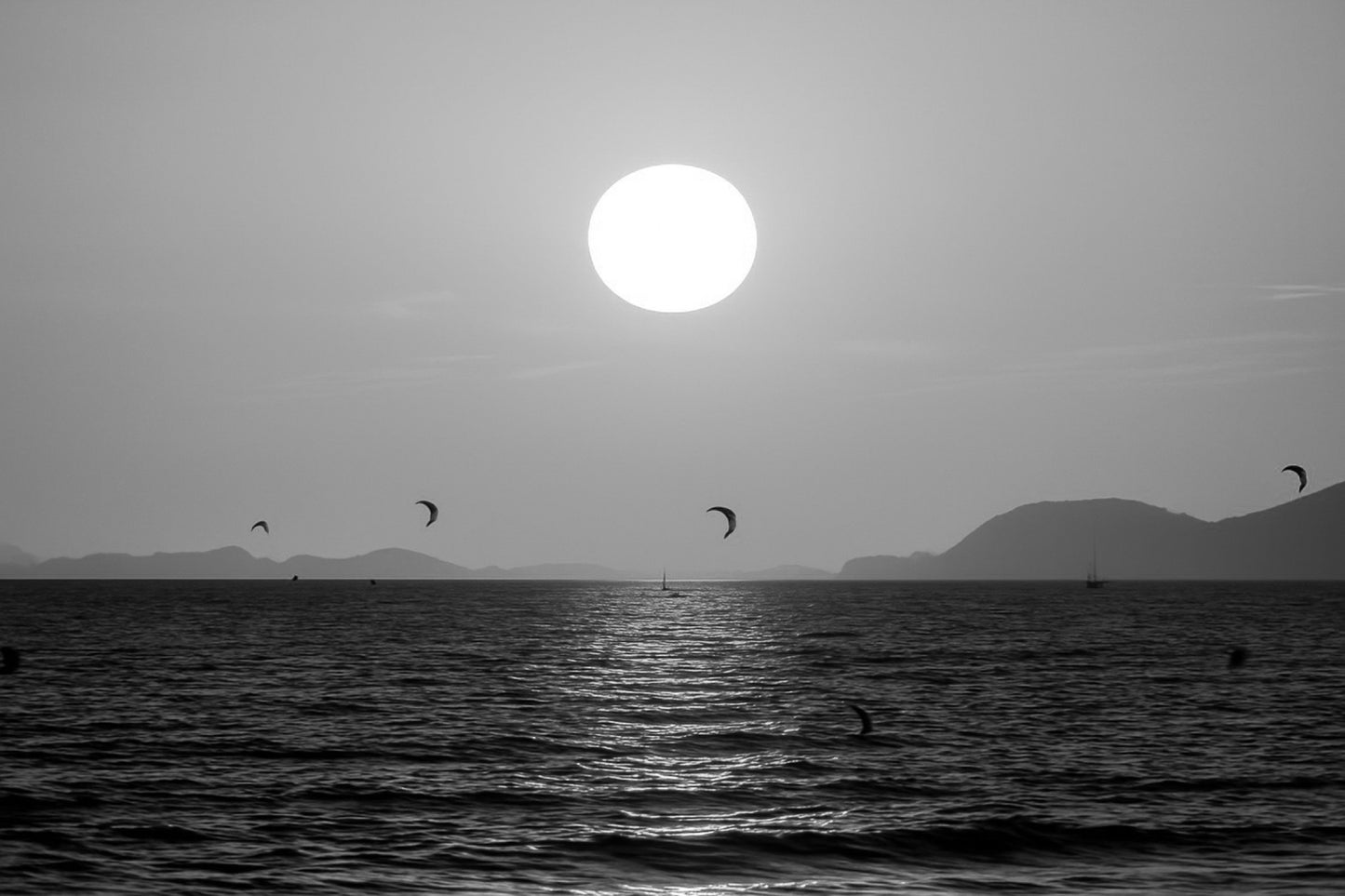 Soleil couchant orange au-dessus de la mer avec des ailes de kitesurf en silhouette à l’Almanarre, noir et blanc