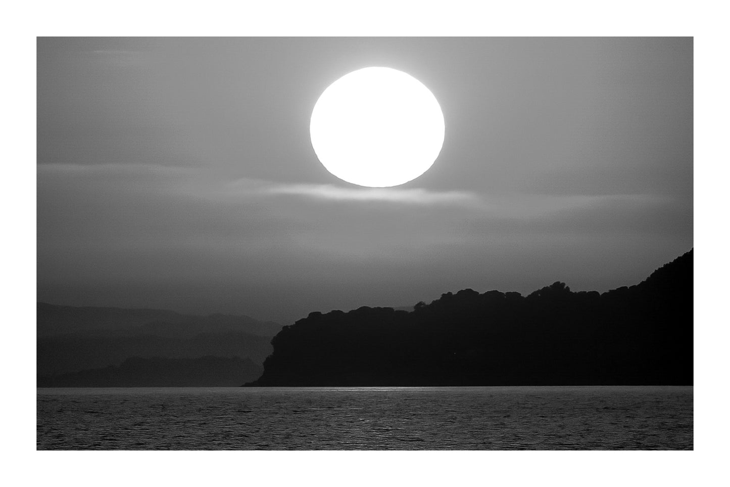 Gros soleil couchant orange au-dessus de la presqu’île de Giens vu depuis la plage de l’Almanarre, noir et blanc avec bordure