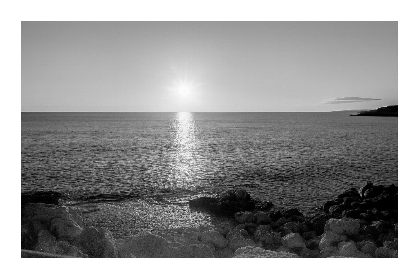 coucher de soleil à Carry-le-Rouet avec reflet doré sur la mer et premiers plans rocheux, noir et blanc avec bordure