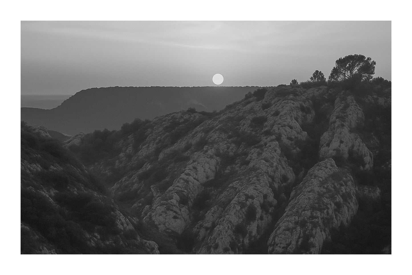 Soleil rond effleurant l’horizon au-dessus d’un vallon de roches blanches, teintes orange depuis le barrage de Bimont, noir et blanc avec bordure