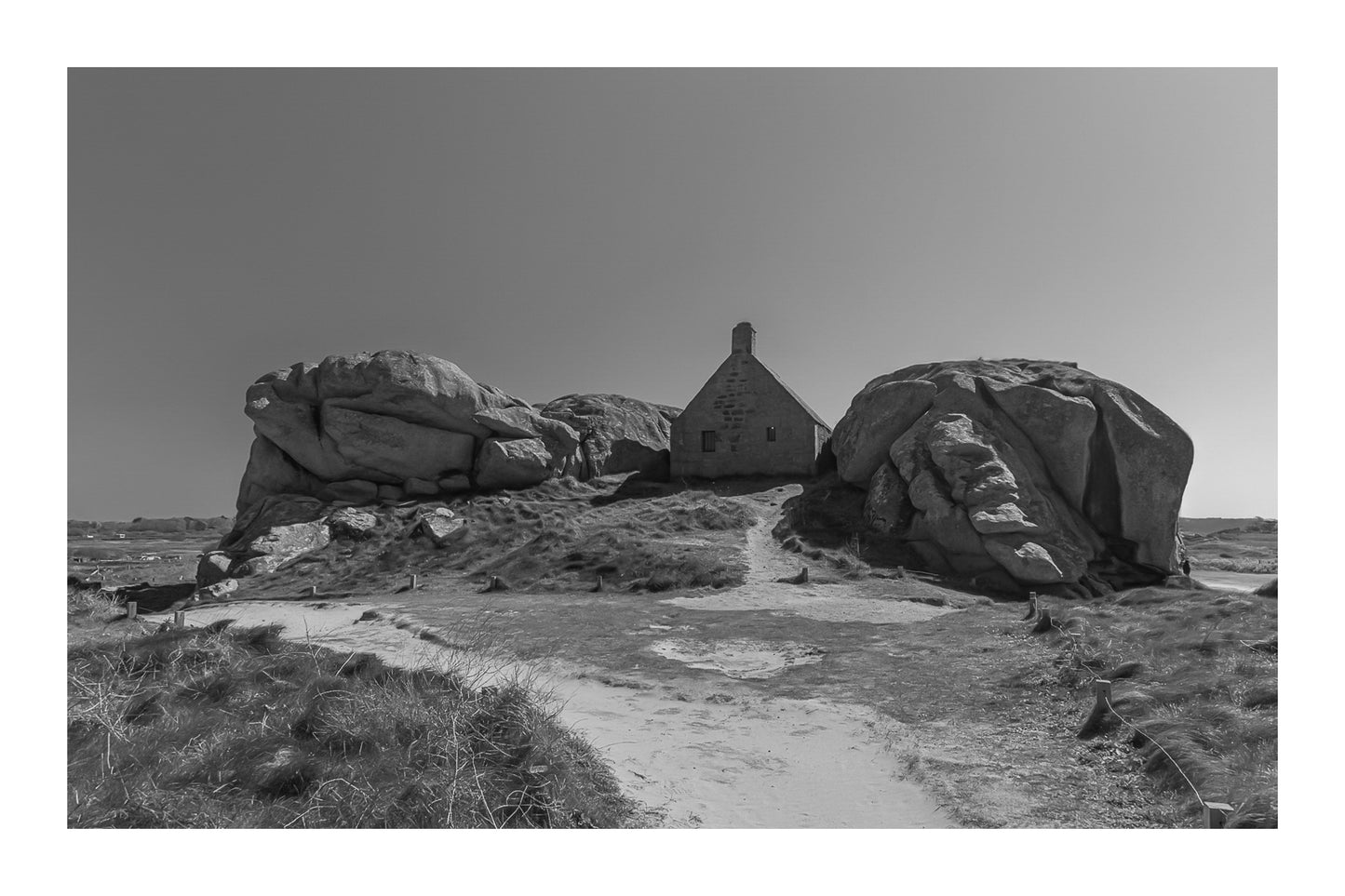 Façade de la maison des gardes encadrée par deux rochers monumentaux, Meneham (Kerlouan), noir et blanc avec bordure