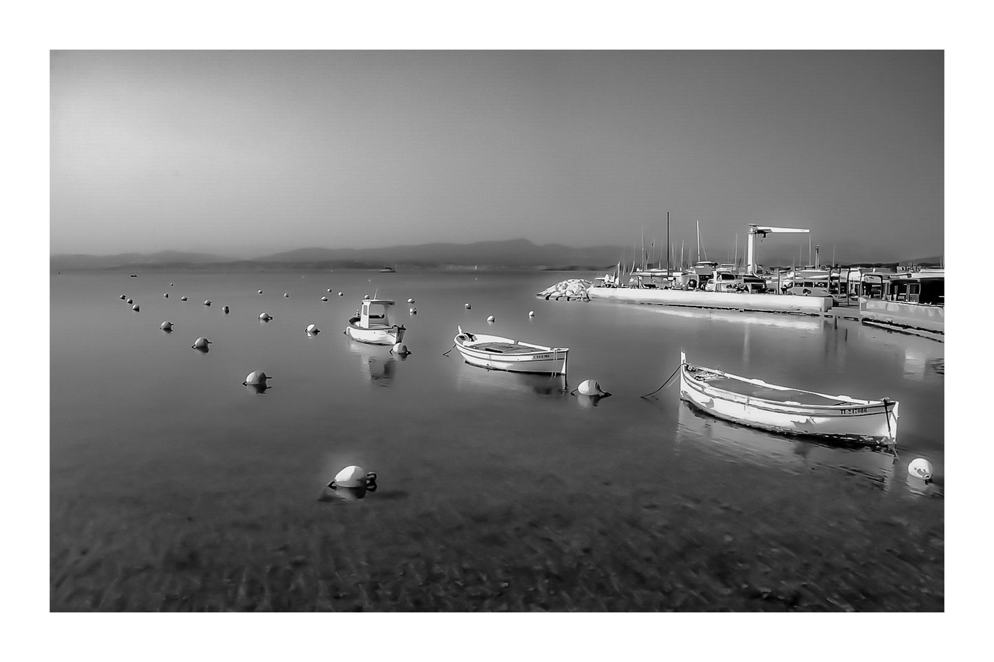 Barques au mouillage face au quai et aux mats du port du Brusc, fin de journée, noir et blanc avec bordure