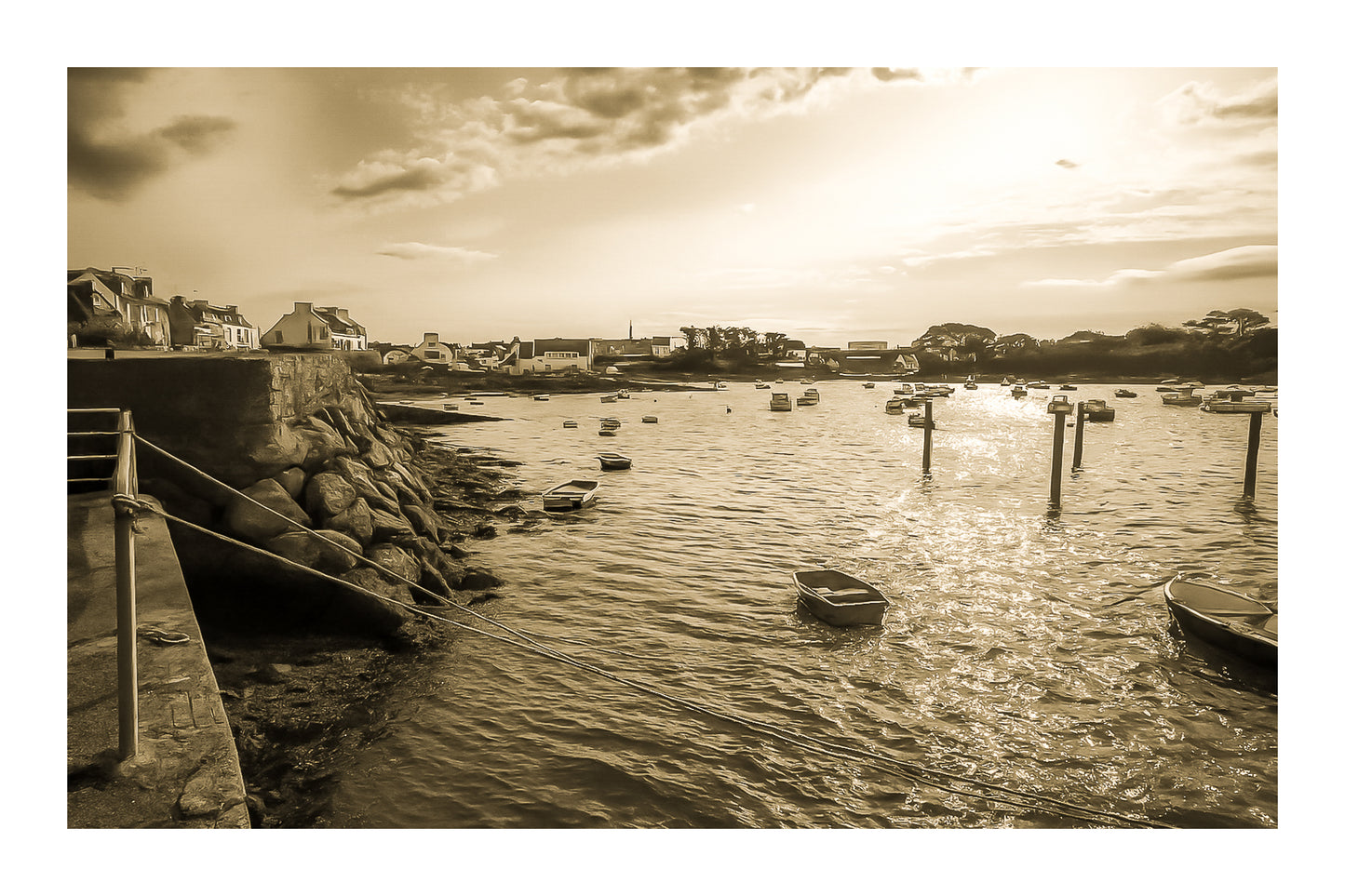 Vue du port de Portsall au coucher du soleil, muret de pierre et rochers au premier plan, petites barques au mouillage sur mer dorée, vintage avec bordure