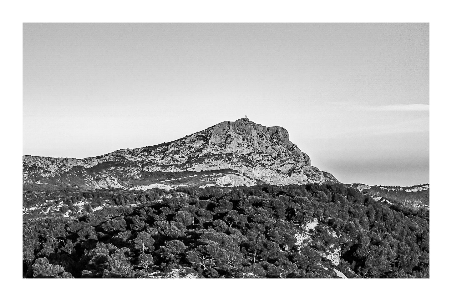 Crête de la Sainte-Victoire entièrement dorée par le soleil au-dessus d’une mer de pins, noir et blanc avec bordure