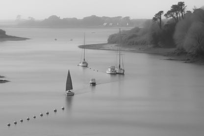 Large vue d’un estuaire breton avec une petite voile rouge et des bouées alignées, noir et blanc