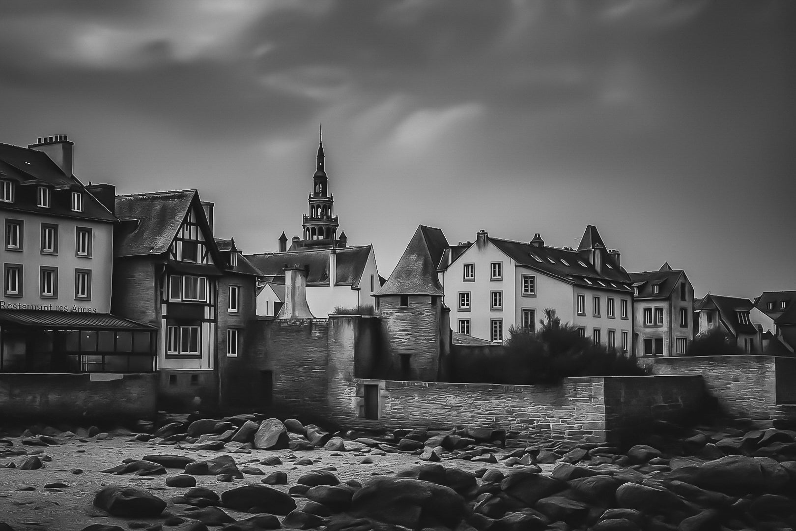 Vue des remparts et des maisons de Roscoff, clocher au loin et grève rocheuse au premier plan, noir et blanc