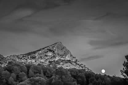 Lune jaune se levant près de la montagne Sainte-Victoire, ciel bleu aux nuages roses, pins en premier plan au crépuscule, noir et blanc