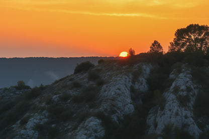 Demi-soleil disparaissant derrière une crête et des pins, ciel incandescent au barrage de Bimont