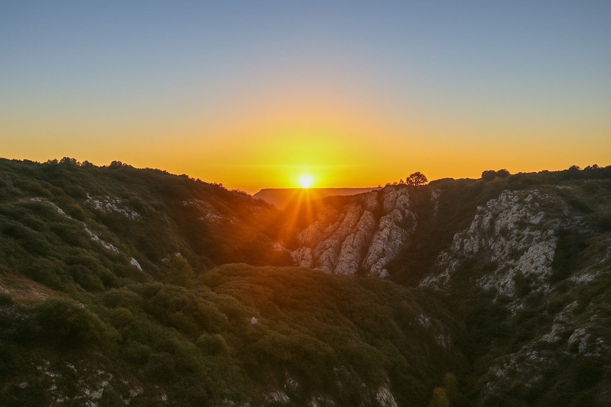 Étoile solaire à l’horizon avec faisceaux lumineux au centre d’un cirque rocheux, vue panoramique depuis Bimont