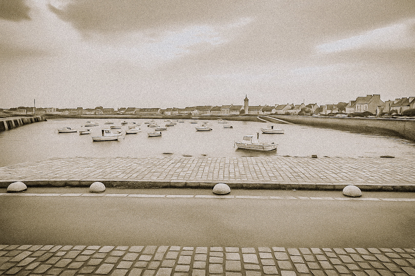 Port de Roscoff en traitement sépia, pavés au premier plan, barques au mouillage et môle au loin