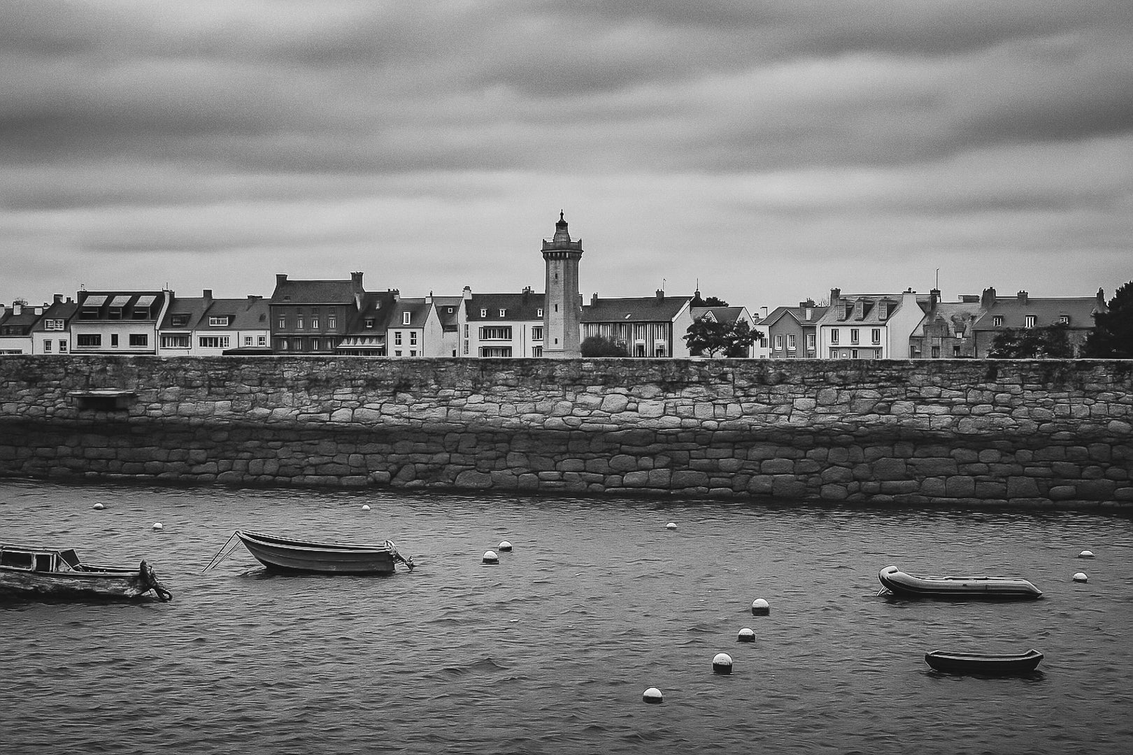 Vue du bassin de Roscoff, jetée en granit, bouées et embarcations avec une tour/clé de clocher en arrière-plan, noir et blanc