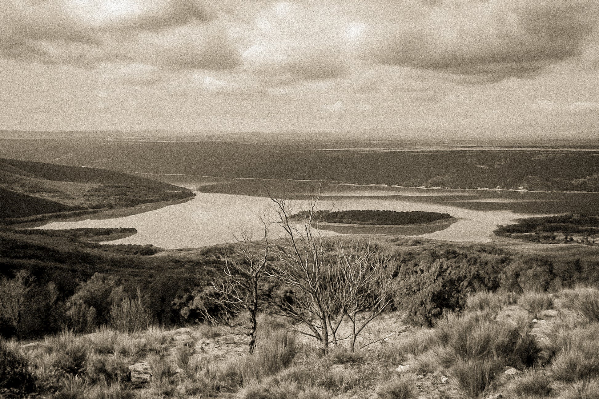 Vue panoramique sur le lac de Sainte-Croix, bras d’eau sinueux et collines provençales sous un ciel nuageux, vintage
