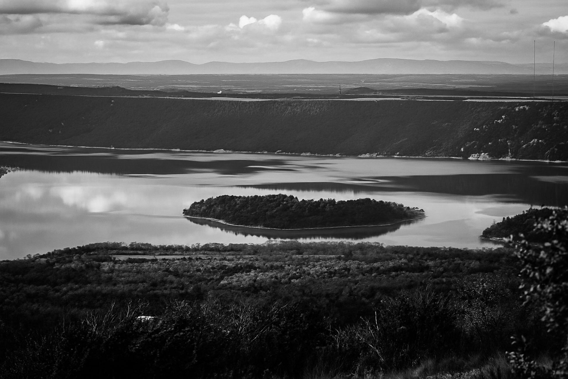 Îlot boisé flottant au centre du lac de Sainte-Croix, eaux calmes et reliefs sombres en arrière-plan, noir et blanc