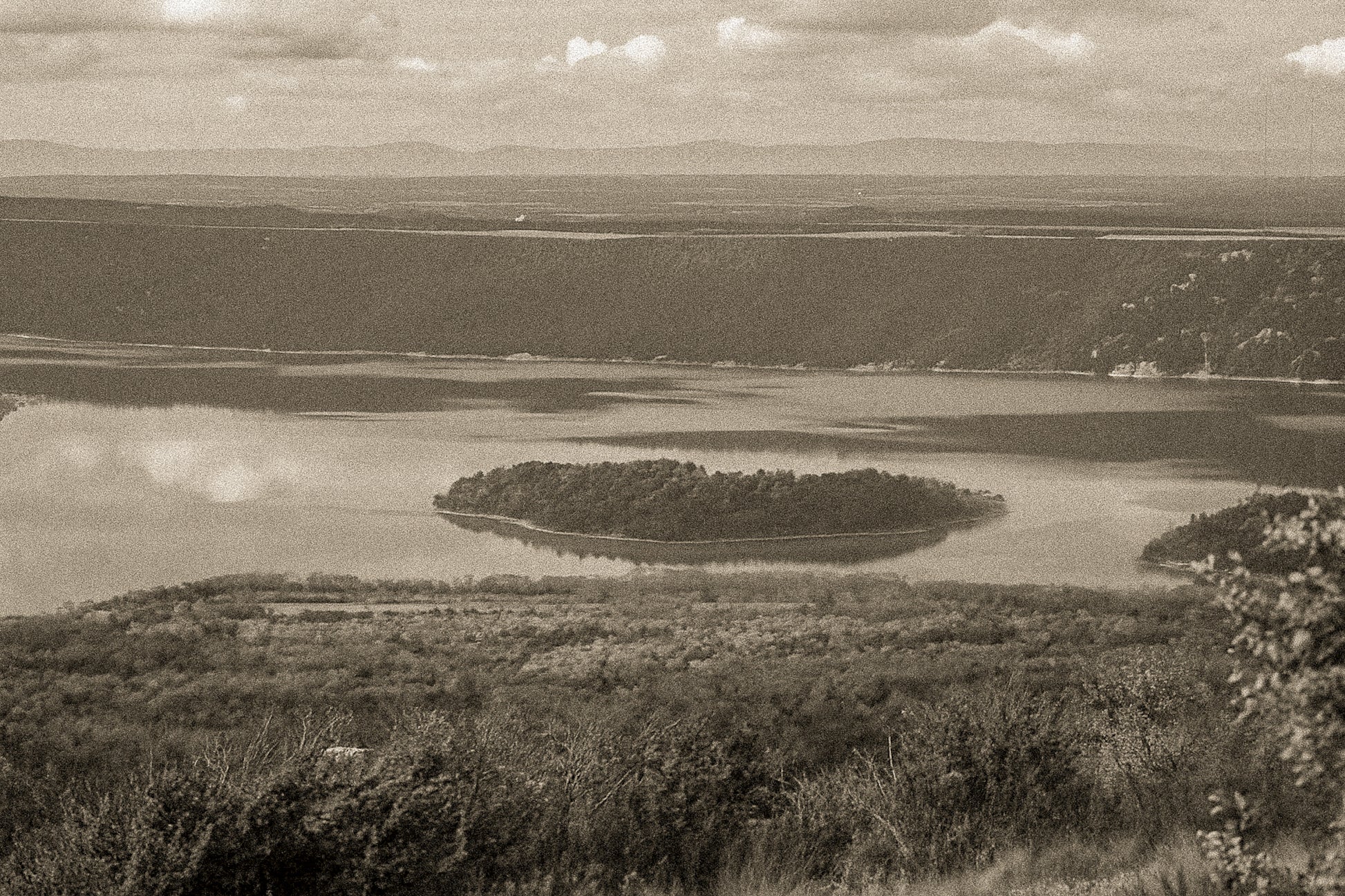 Îlot boisé flottant au centre du lac de Sainte-Croix, eaux calmes et reliefs sombres en arrière-plan, vintage