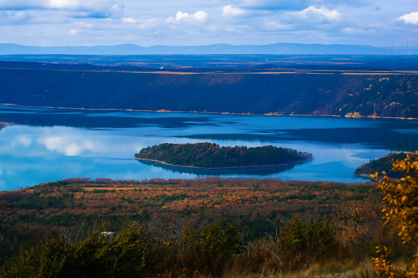 Îlot boisé flottant au centre du lac de Sainte-Croix, eaux calmes et reliefs sombres en arrière-plan