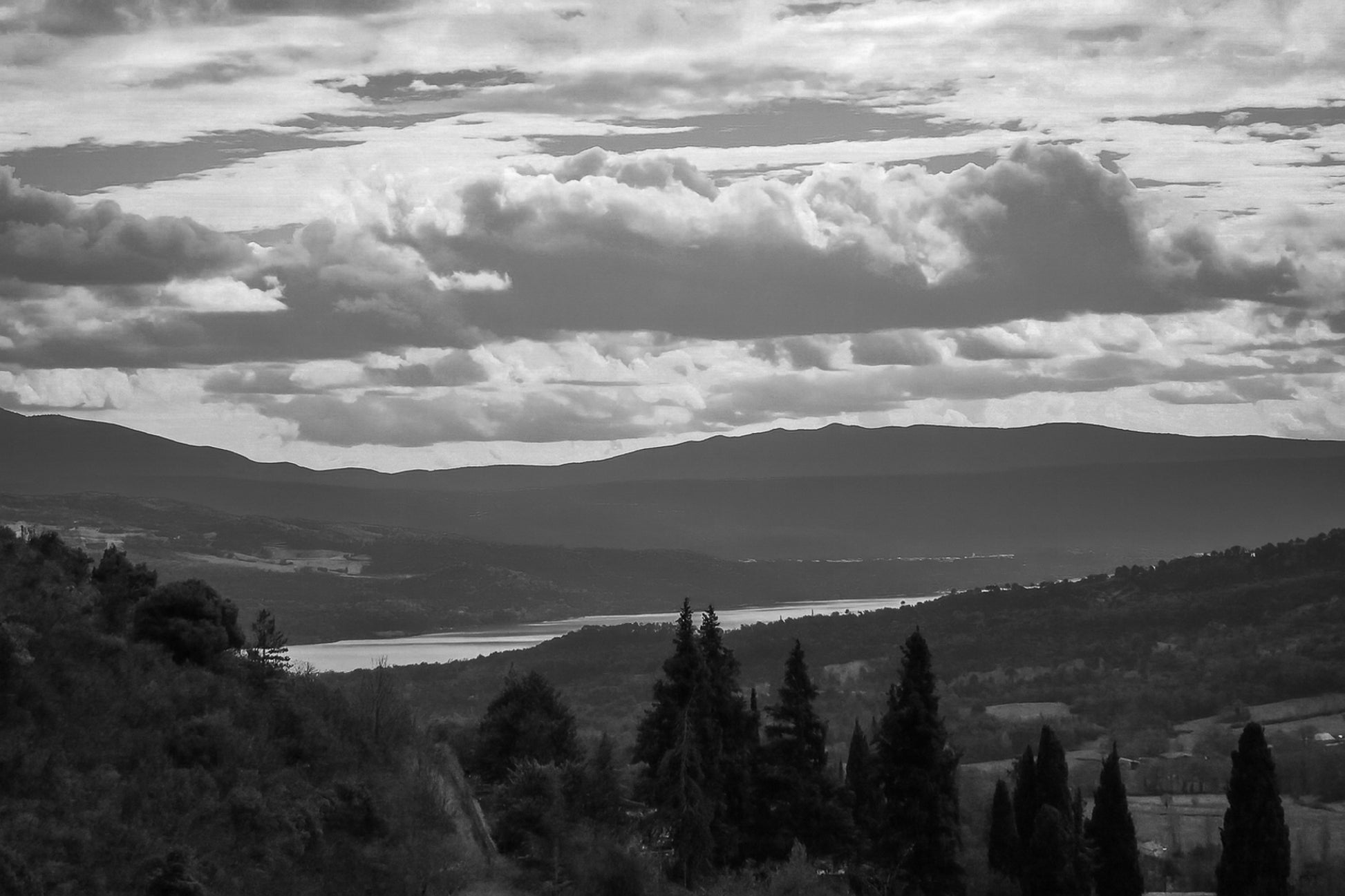 Vue lointaine sur le lac de Sainte-Croix entouré de collines, sous un ciel de nuages contrastés, noir et blanc