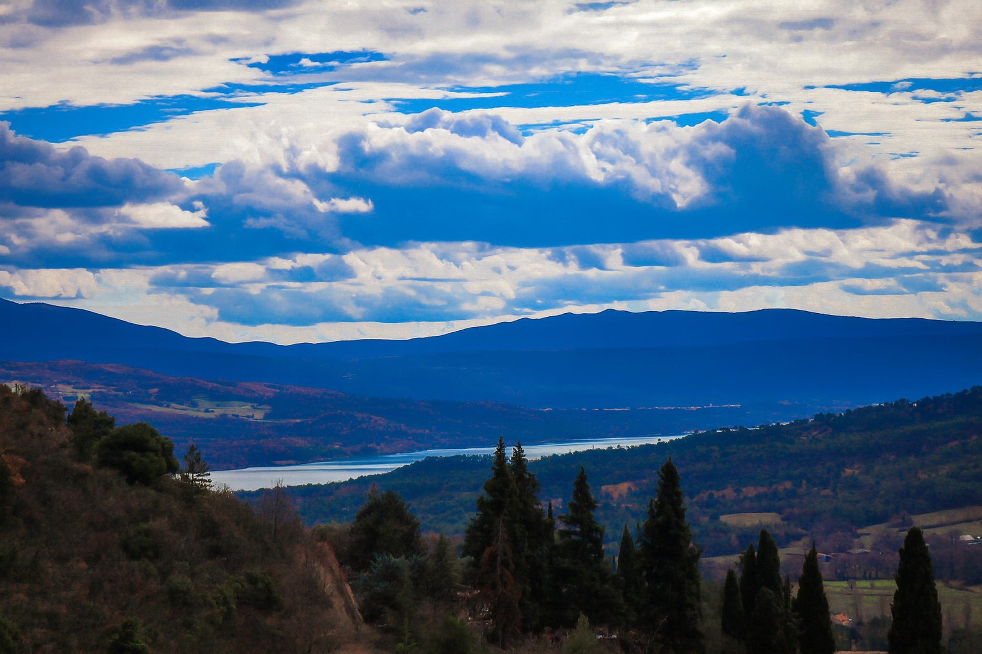 Vue lointaine sur le lac de Sainte-Croix entouré de collines, sous un ciel de nuages contrastés