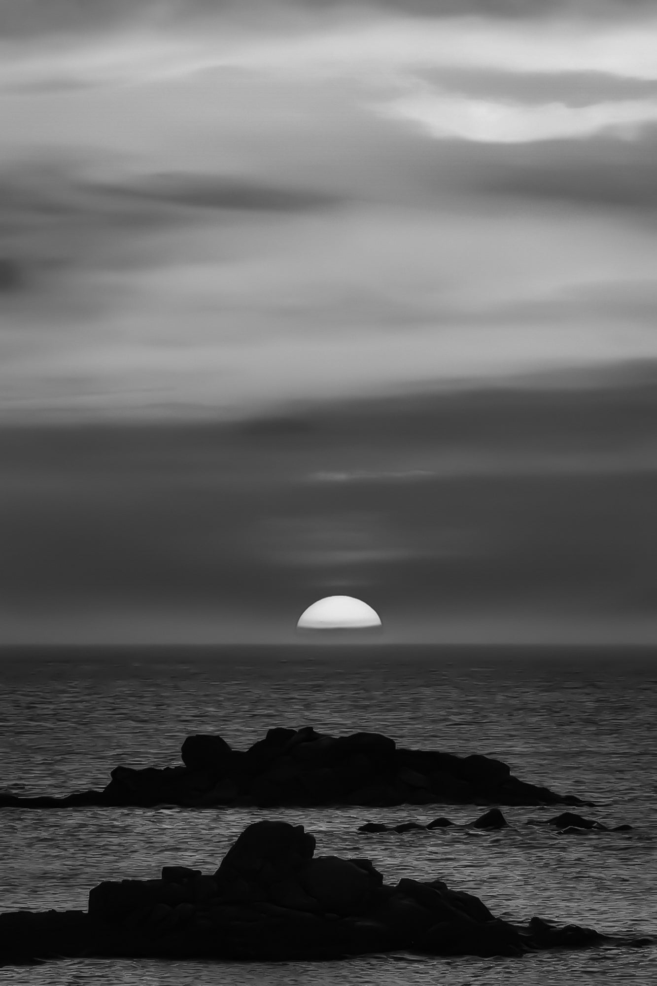 Coucher de soleil pastel avec ciel rose, jaune et bleu au-dessus de l’océan et d’îlots rocheux à l’Aber Wrac’h, noir et blanc