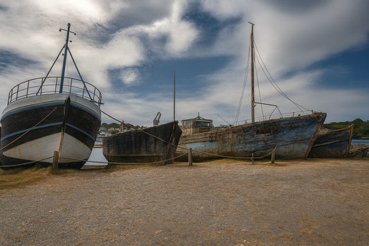 Trois bateaux en bois alignés sur la grève à Camaret, ciel nuageux et port en arrière-plan