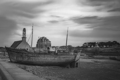 Épave bleue au premier plan devant chapelle et maisons, ciel doré au-dessus du port de Camaret, noir et blanc