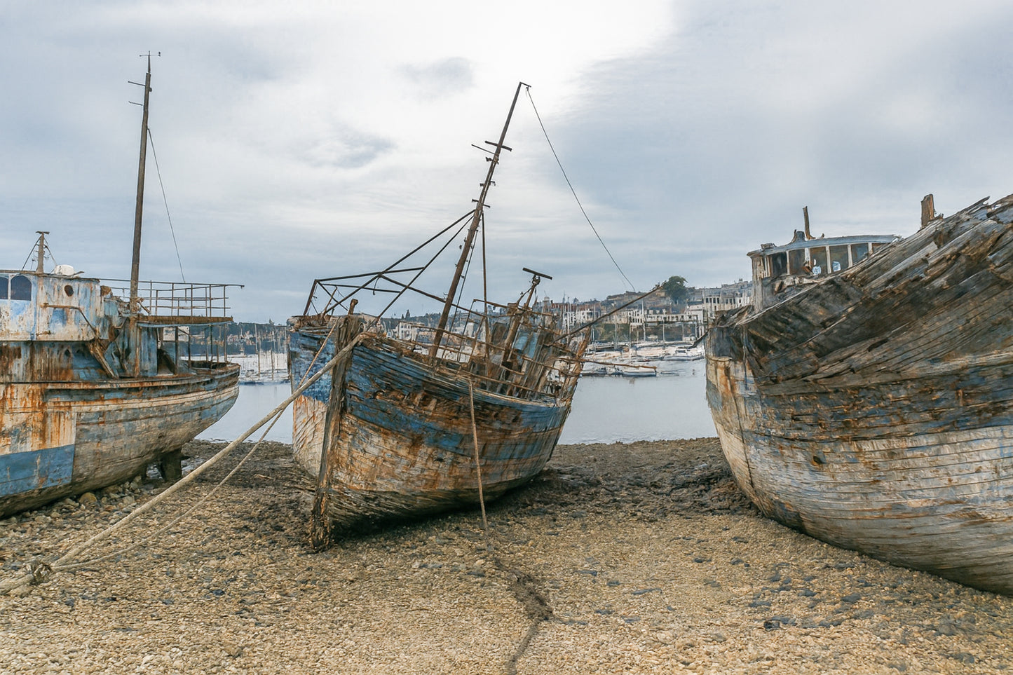 Vieille coque bleue au centre des épaves sur galets, ville de Camaret au fond
