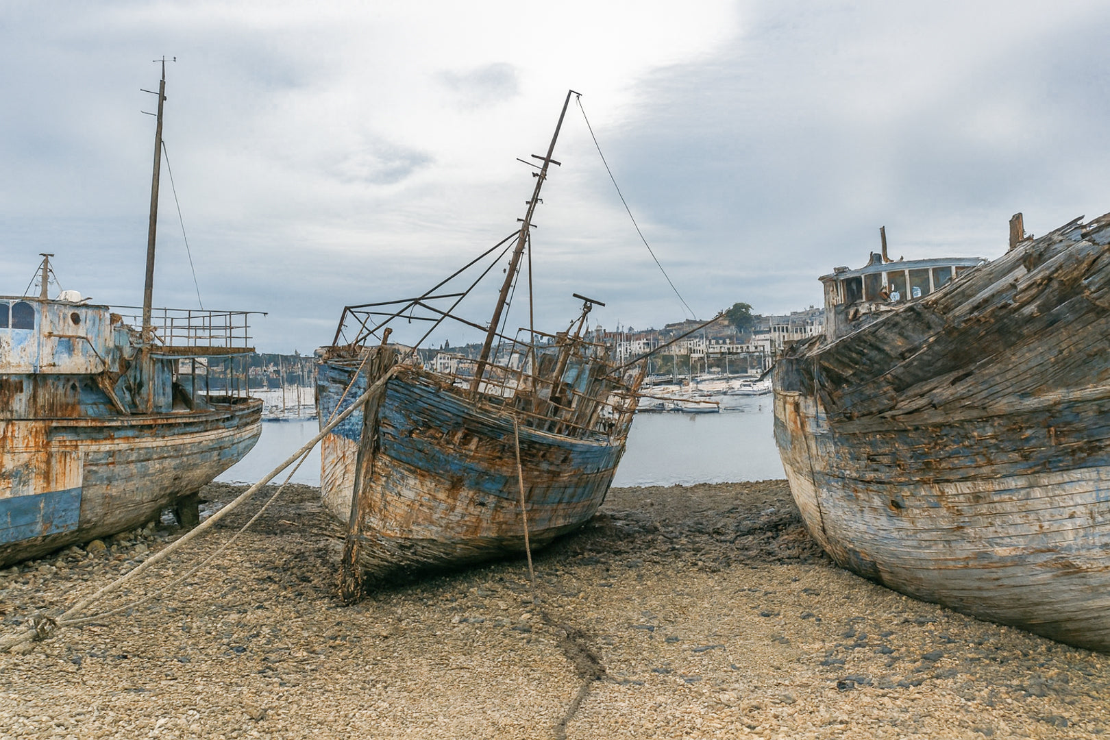 Vieille coque bleue au centre des épaves sur galets, ville de Camaret au fond