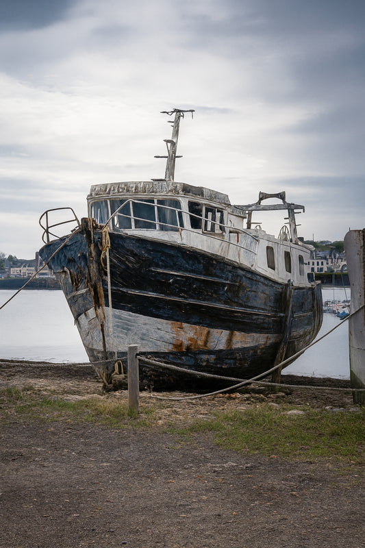 Épave au nez bleu et blanc amarrée par des cordes sur l’estran, ciel couvert au port de Camaret