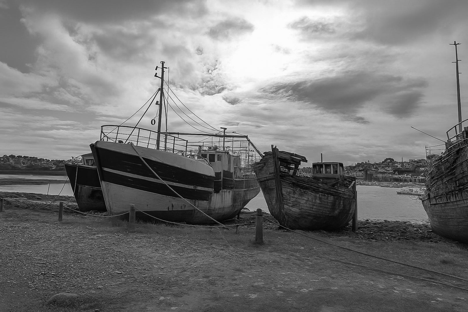 Bateau plus récent sur la gauche et coque déchiquetée à droite sur la grève de Camaret, ciel lumineux, noir et blanc