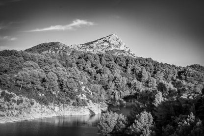 Vue de la montagne Sainte-Victoire dominant une colline de pins et un petit lac en contrebas sous un ciel bleu pur, noir et blanc