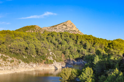 Vue de la montagne Sainte-Victoire dominant une colline de pins et un petit lac en contrebas sous un ciel bleu pur
