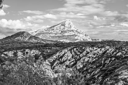Panorama de la Sainte-Victoire et de ses vallons rocheux couverts de garrigue sous un ciel bleu parsemé de nuages, noir et blanc