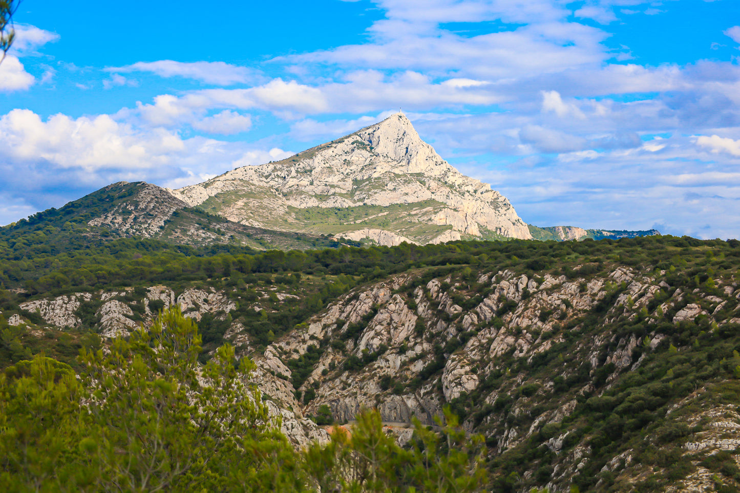 Panorama de la Sainte-Victoire et de ses vallons rocheux couverts de garrigue sous un ciel bleu parsemé de nuages.