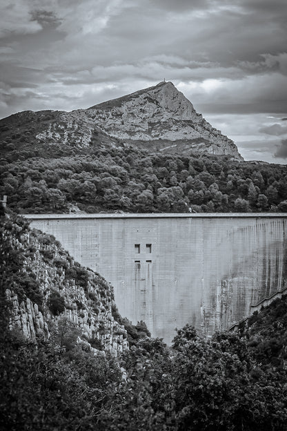 Barrage massif au premier plan avec la Sainte-Victoire en arrière-plan, forêt méditerranéenne et ciel nuageux, noir et blanc