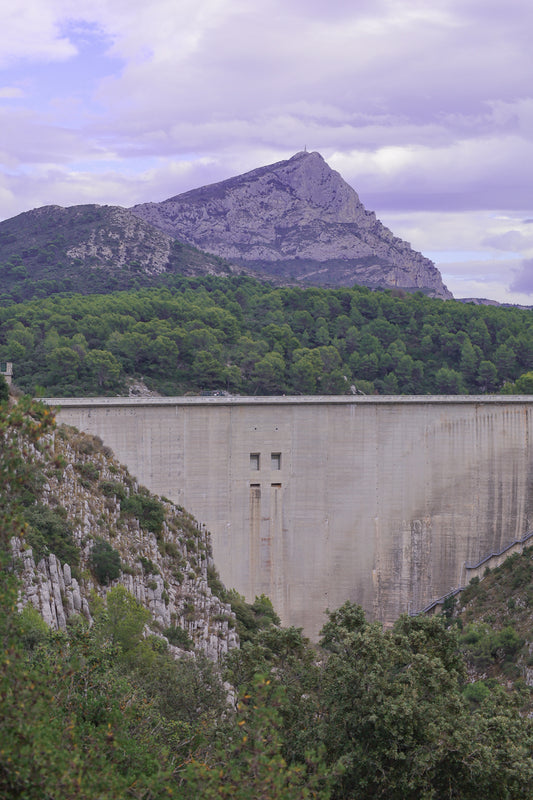 Barrage massif au premier plan avec la Sainte-Victoire en arrière-plan, forêt méditerranéenne et ciel nuageux.