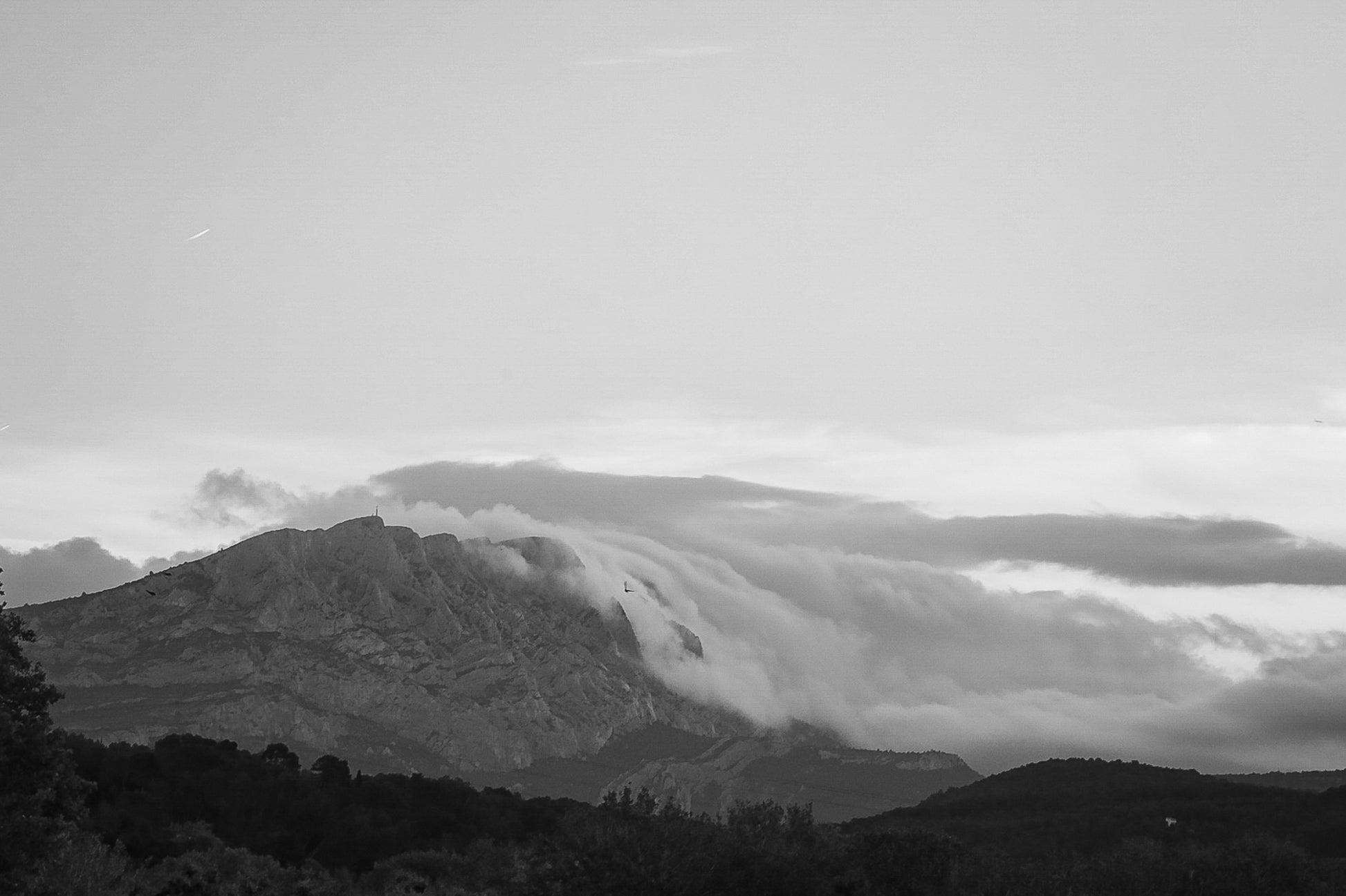 Sainte-Victoire au crépuscule avec nuages en cascade sur les crêtes, avant-plans sombres de collines et d’arbres, noir et blanc