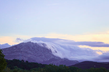 Sainte-Victoire au crépuscule avec nuages en cascade sur les crêtes, avant-plans sombres de collines et d’arbres.