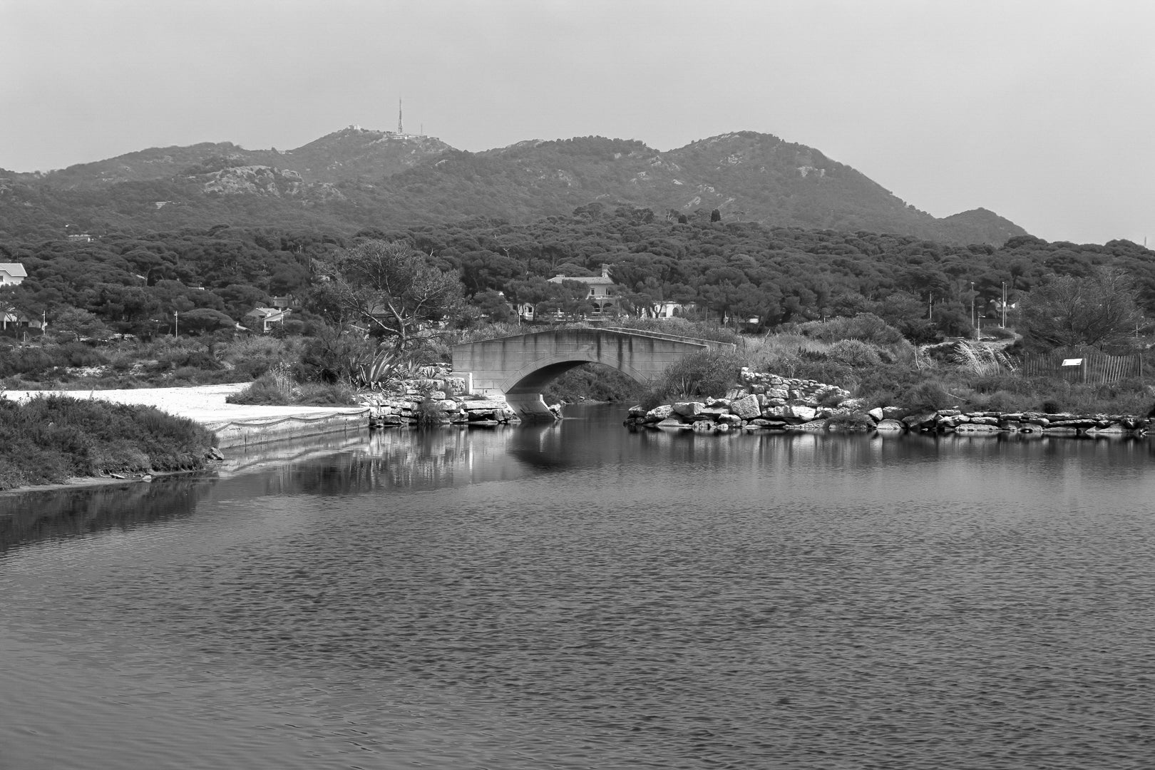 Petit pont en arc sur le canal intérieur des Embiez avec collines en arrière-plan, noir et blanc