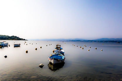 Trois barques alignées dans l’axe, bouées et eau immobile, brume et collines lointaines au Brusc, couleur