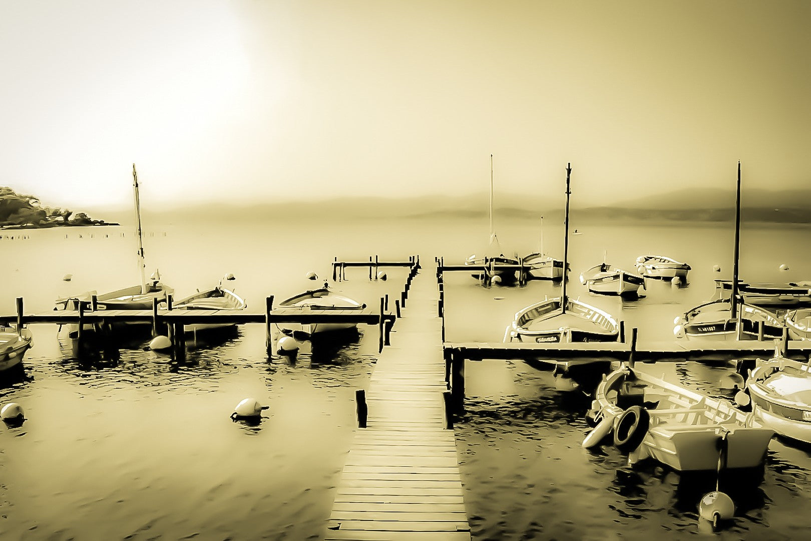Ponton en bois menant à une rangée de barques, mer lisse et brume douce au port du Brusc, look vintage sépia