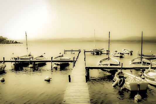 Ponton en bois menant à une rangée de barques, mer lisse et brume douce au port du Brusc, look vintage sépia