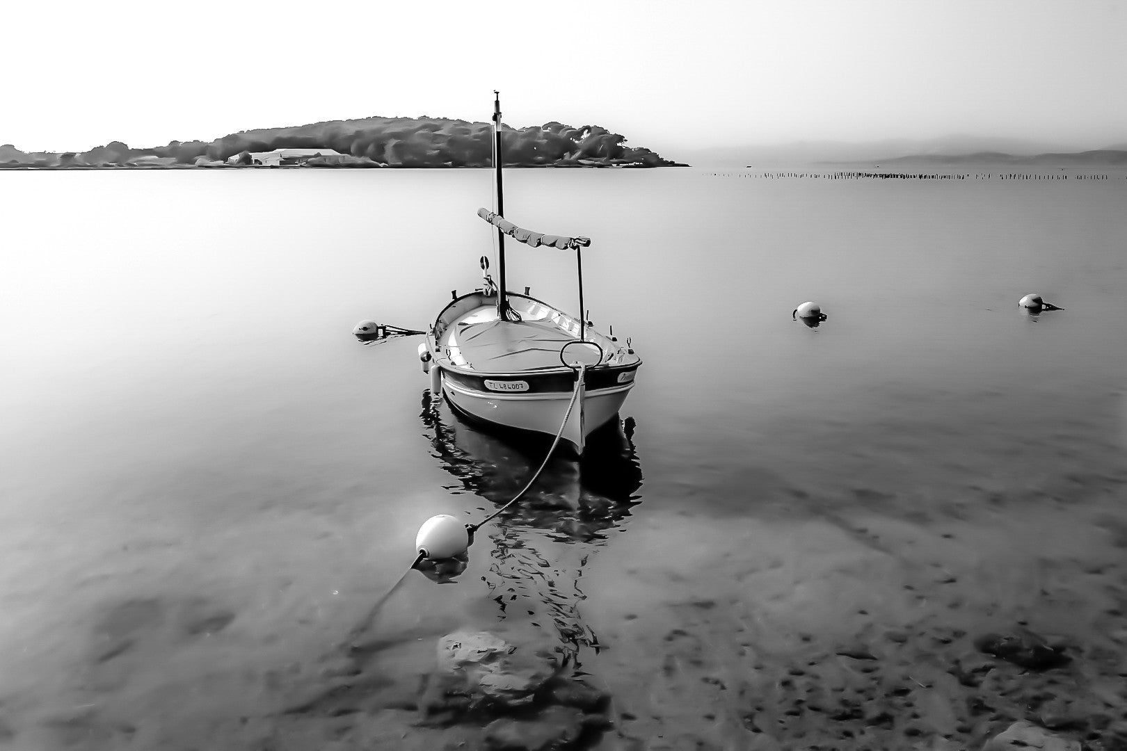 Barque solitaire amarrée avec sa aussière et bouées, reflets sur l’eau, port du Brusc, noir et blanc