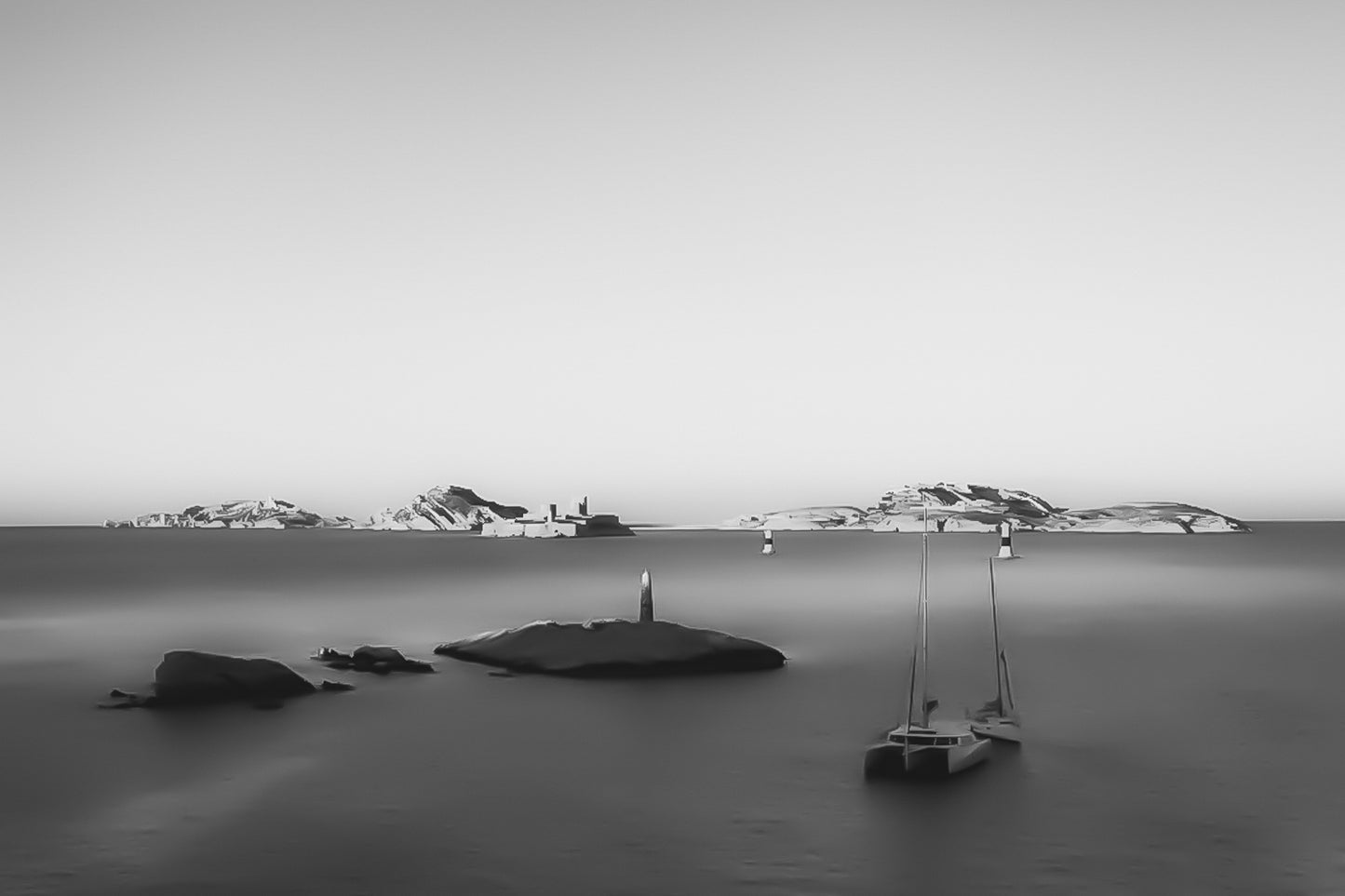 Longue exposition depuis la corniche : balise et bateaux au premier plan, Château d’If et îles du Frioul illuminés par le coucher de soleil, noir et blanc