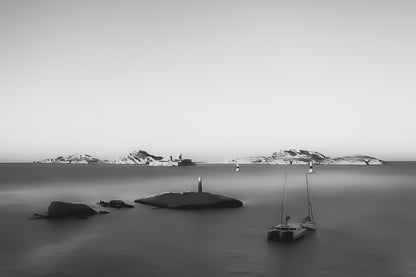 Longue exposition depuis la corniche : balise et bateaux au premier plan, Château d’If et îles du Frioul illuminés par le coucher de soleil, noir et blanc