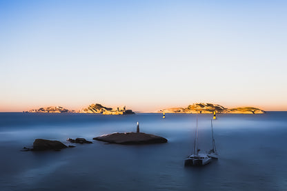 Longue exposition depuis la corniche : balise et bateaux au premier plan, Château d’If et îles du Frioul illuminés par le coucher de soleil