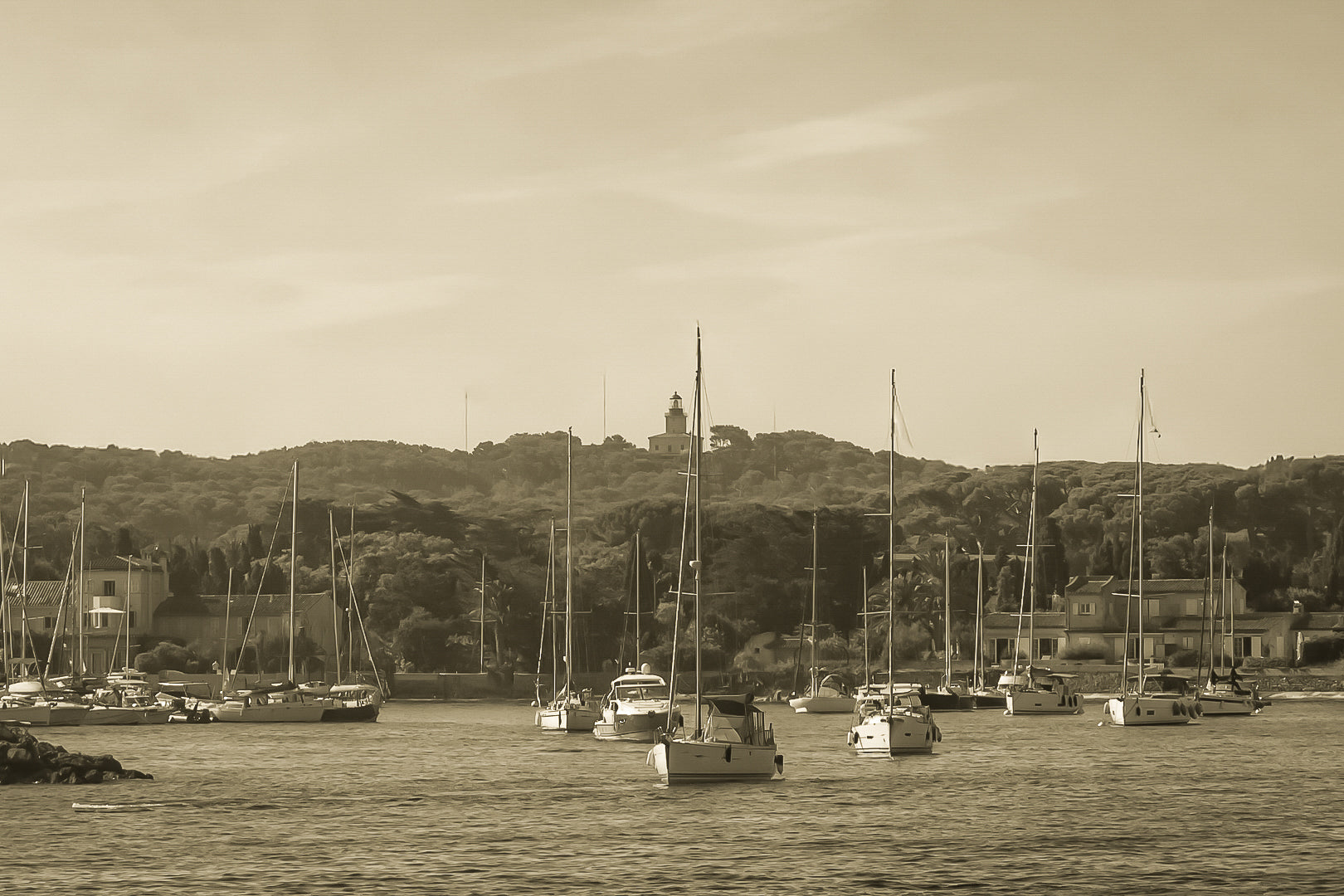 Voiliers au mouillage devant le village de Porquerolles avec le phare sur la colline, ciel bleu et pinède méditerranéenne, vintage