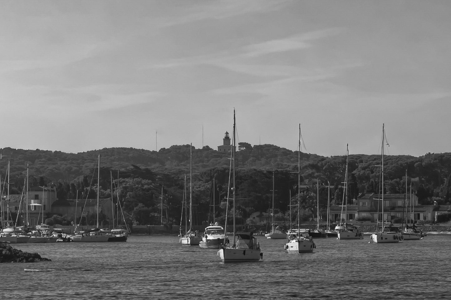 Voiliers au mouillage devant le village de Porquerolles avec le phare sur la colline, ciel bleu et pinède méditerranéenne, noir et blanc
