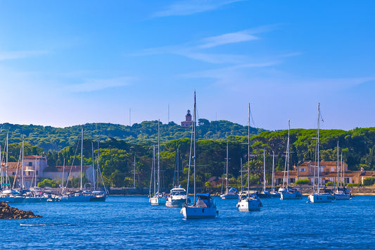 Voiliers au mouillage devant le village de Porquerolles avec le phare sur la colline, ciel bleu et pinède méditerranéenne
