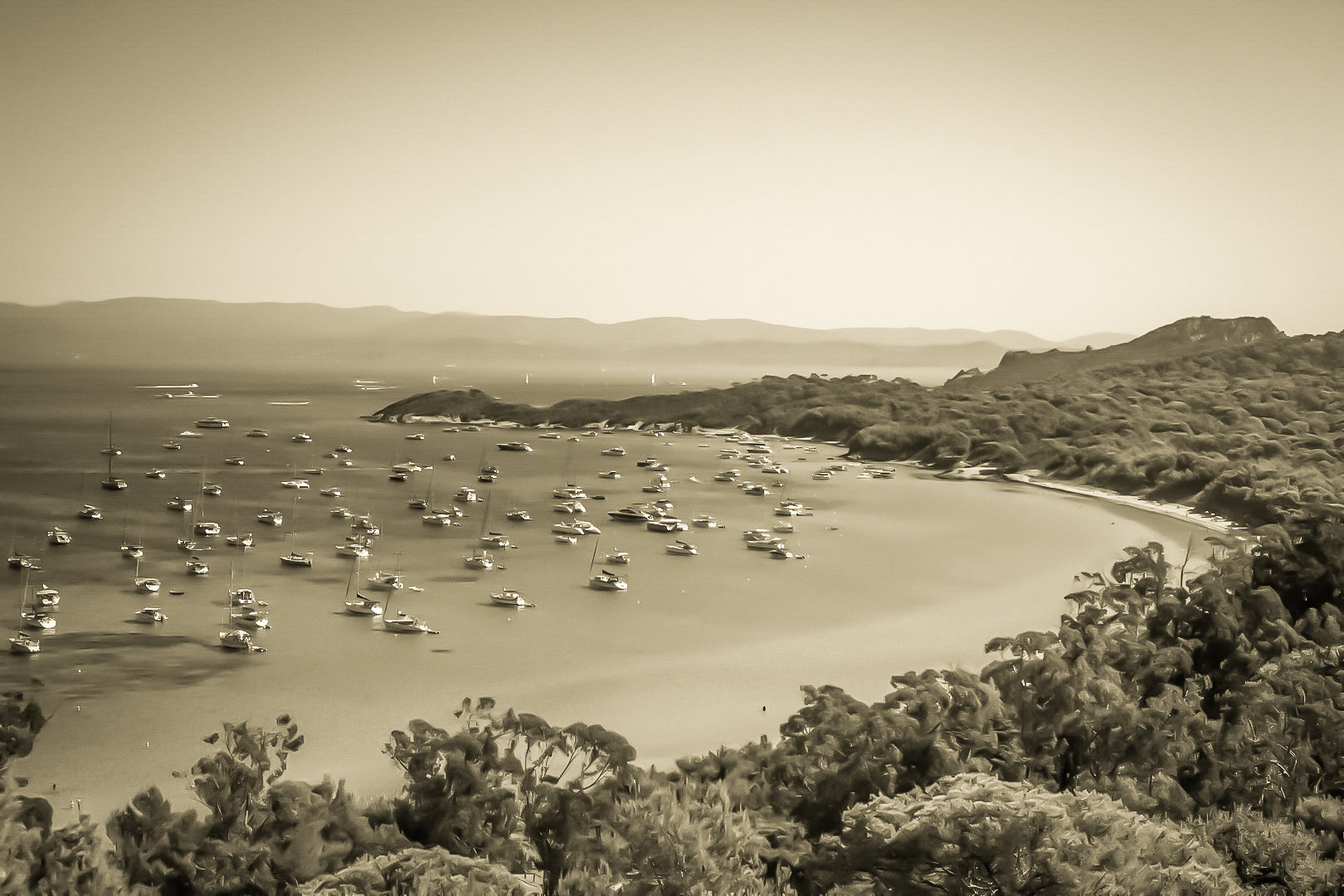 Vue plongeante sur la grande baie de Porquerolles avec de nombreux bateaux ancrés dans une eau turquoise sous un ciel d’été, vintage