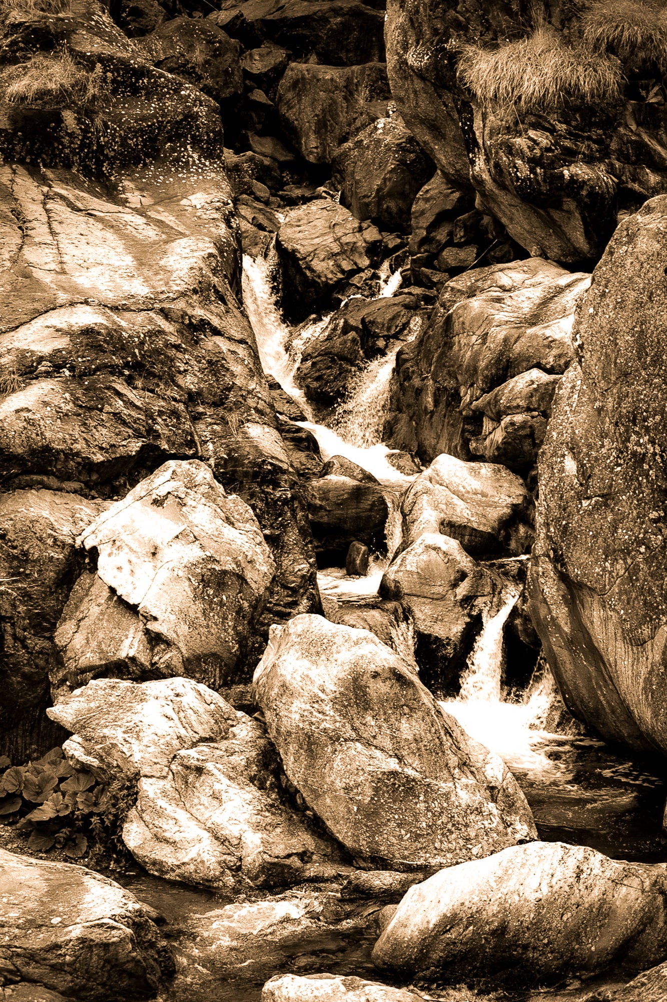 Cascade du Ray entre de gros blocs rocheux, eau qui s’écoule en marches successives dans un style vintage sépia.